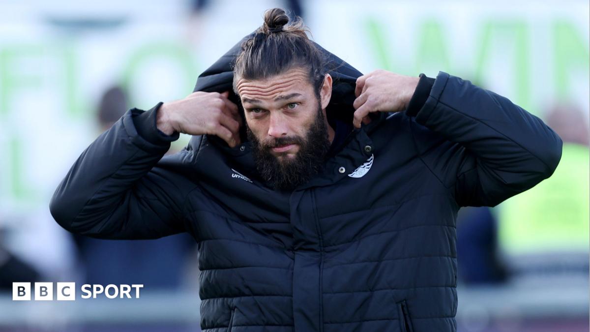 Andy Carroll pulls a hood over his head while walking to the bench during a Dagenham match
